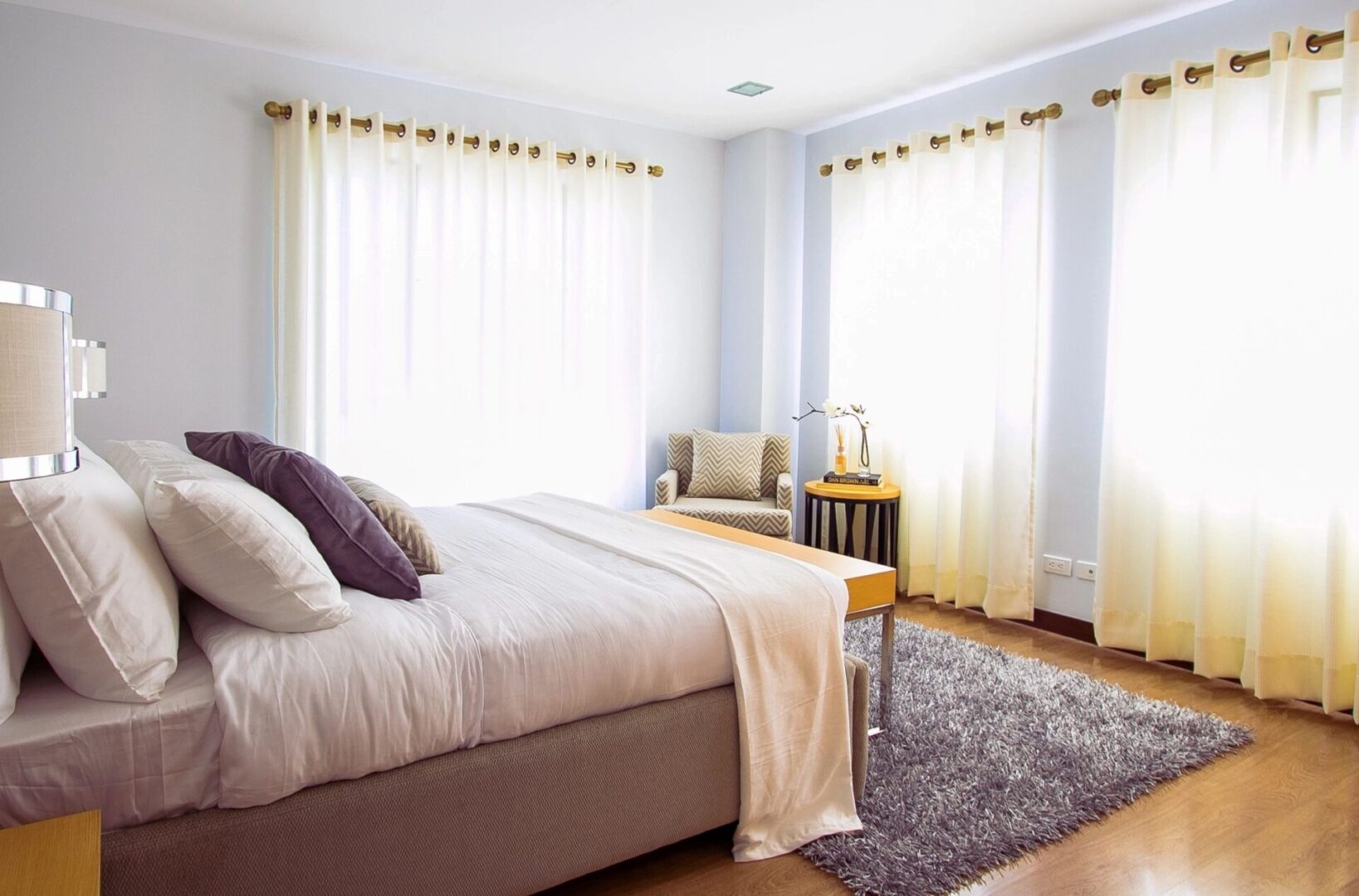 Bright bedroom with large windows, cozy bed, and soft curtains.