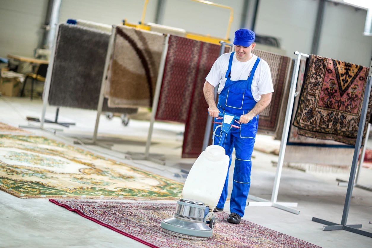 Worker cleaning a carpet with a floor buffer machine.