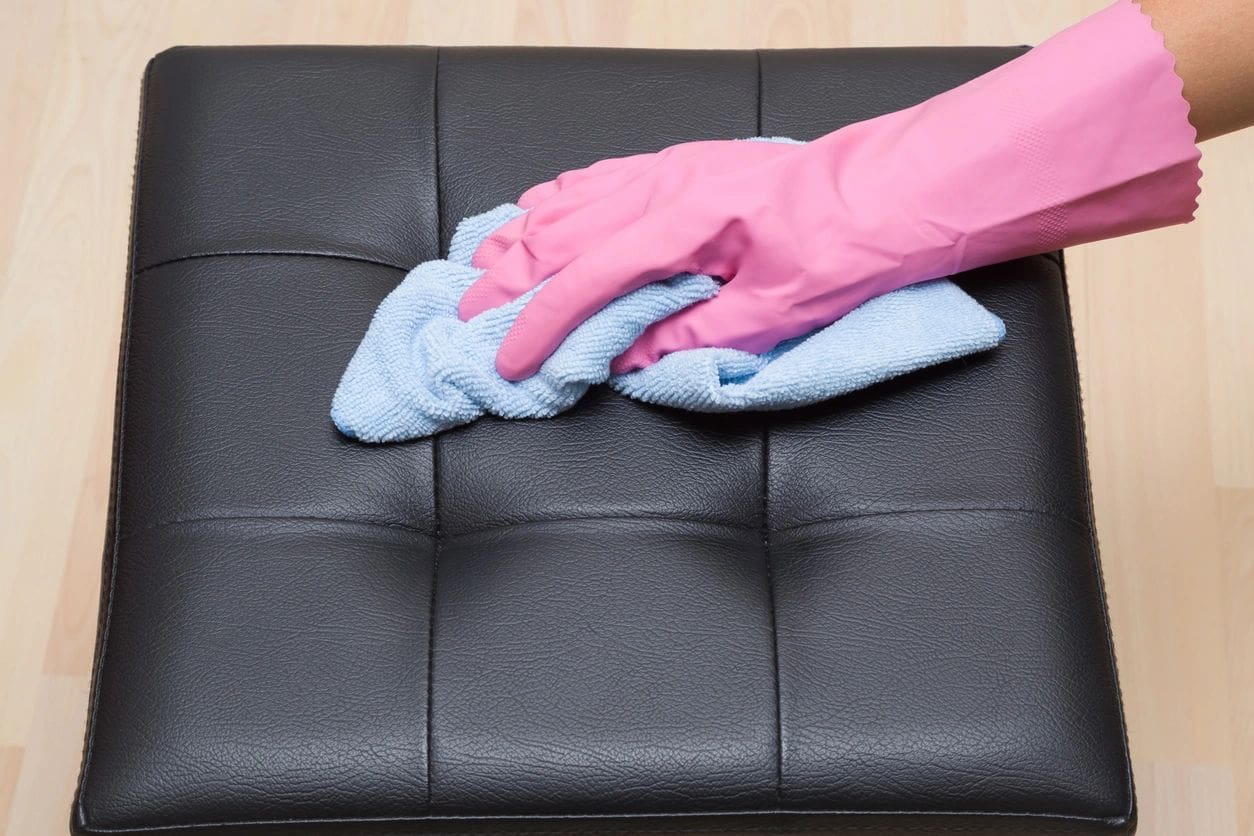 Hand wearing pink gloves cleaning a black leather surface with a blue cloth.