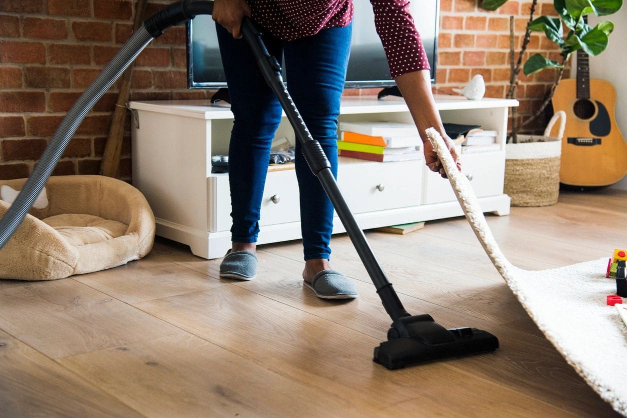 Person vacuuming a hardwood floor in a cozy living room.