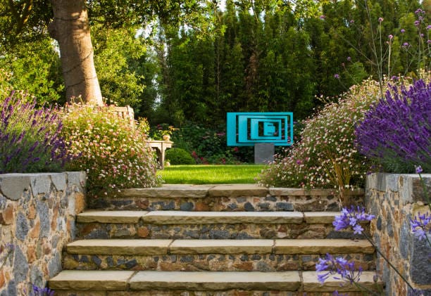 A serene garden pathway with stone steps and a blue bench surrounded by greenery.