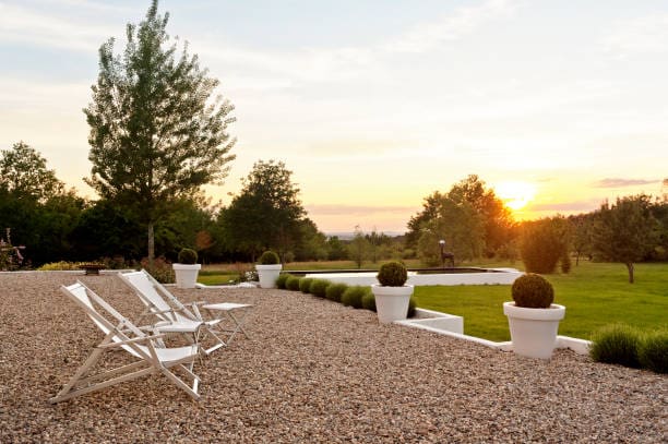 Sunset view over a peaceful patio with white chairs and potted plants.