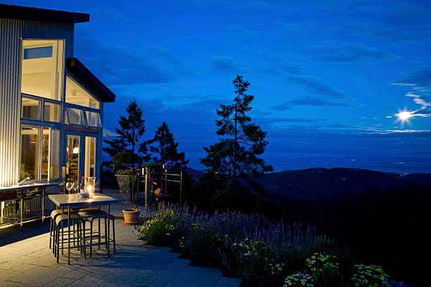 Cozy outdoor patio lit warmly against a twilight sky with trees and distant hills.