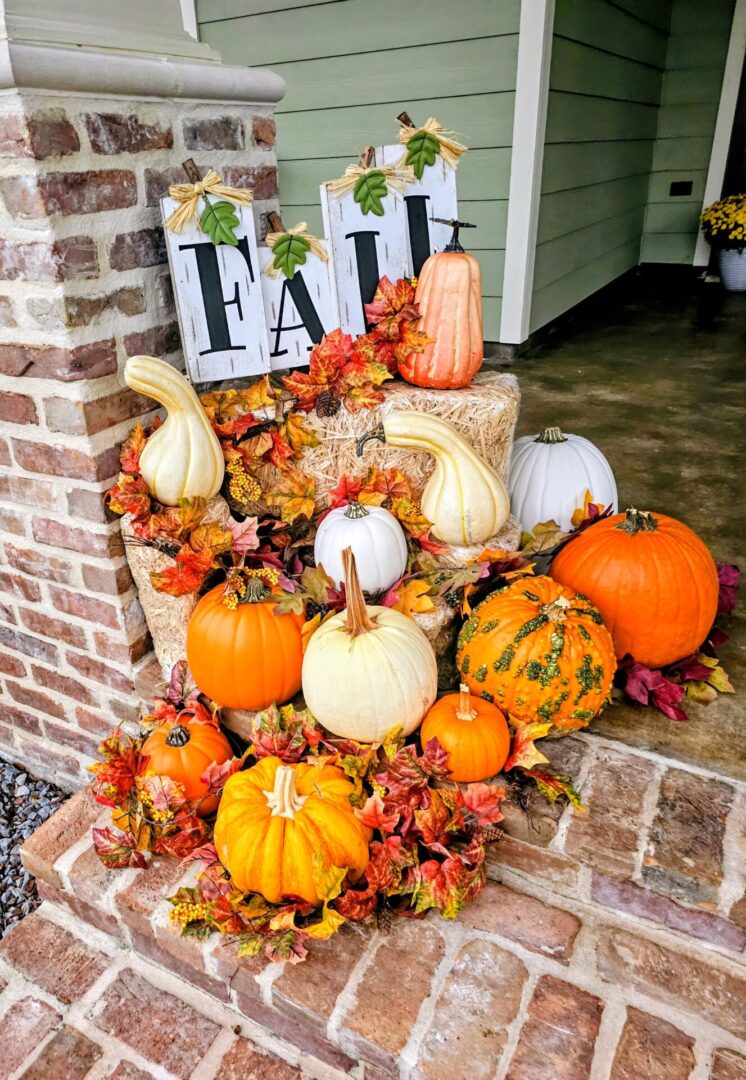 A festive fall display with pumpkins and autumn leaves on a porch.