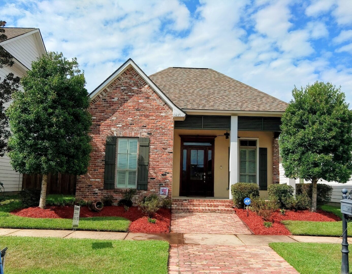 Charming brick house with a gabled roof and front porch under blue sky.