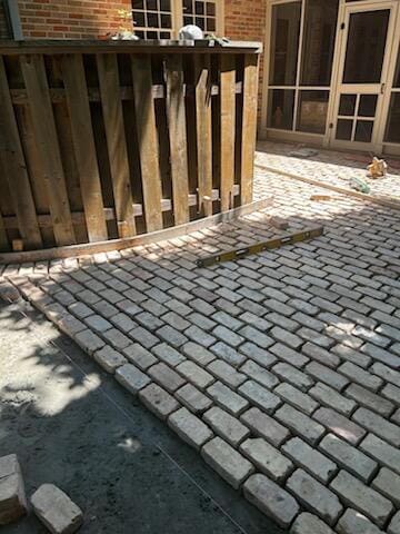 Sunlit cobblestone pathway next to a wooden fence.